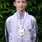 Chłopiec ma na szyi Złoty medal w Taekwondo na tle winorośli.Złoty medal w Taekwondo