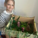 Dziewczynka pokazuje swoją ręcznie wykonaną makietę ogrodu.