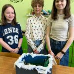 Trójka uczniów prezentuje ręcznie wykonaną makietę ogrodu inspirowaną lekturą "Tajemniczy ogród".