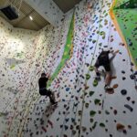 Dwójka uczniów wspina się na wysoką ściankę wspinaczkową.