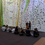 Uczniowie słuchają instrukcji na ściance wspinaczkowej.